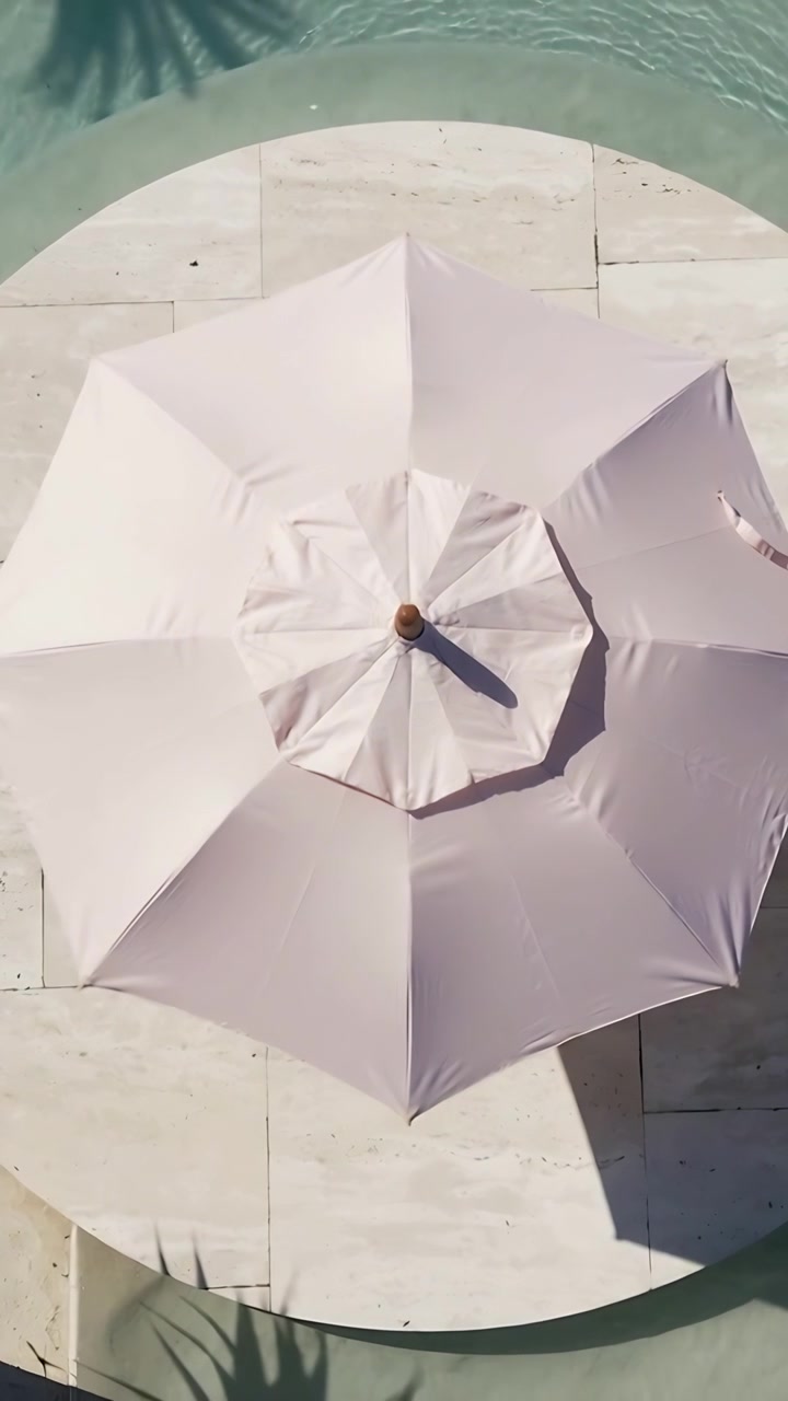 Video verticale: La telecamera si allontana rivelando un ombrellone rosa su una lastra, mostrando una piscina e l'ombra di una palma.