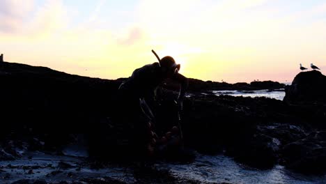 Cámara-Lenta-De-Un-Pescador-Submarino-Tomando-Su-Bolsa-De-Pescado-Después-De-Un-Día-De-Pesca-Submarina,-Silueta-Al-Atardecer-Frente-A-La-Costa-De-Chile-Maule-Duao-Región-Momento-De-Calma-Y-Relajación