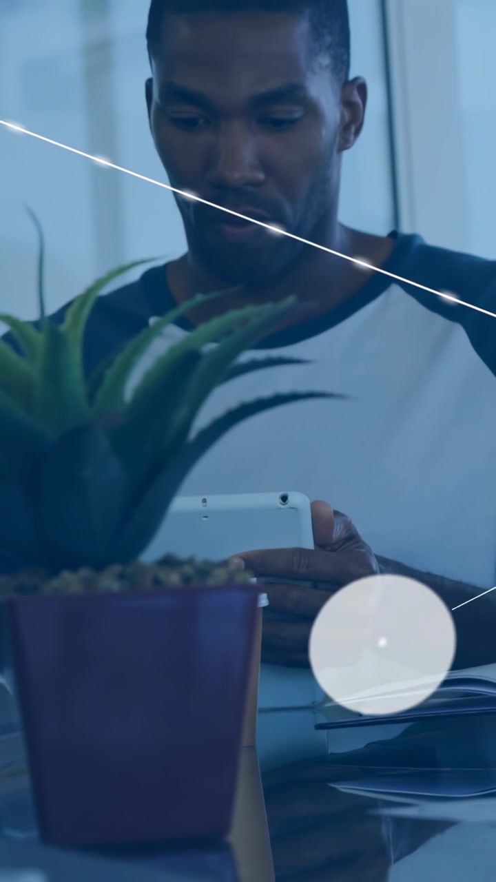 Uomo di mezza età seduto al tavolo che usa un tablet, con icone di rete tecnologiche che si diffondono intorno al tablet e una pianta.
