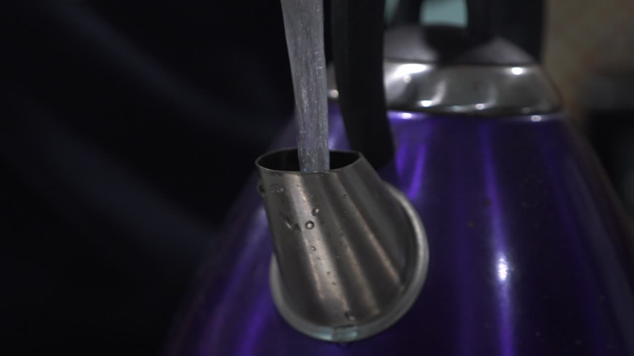 el agua corriente del grifo de la cocina llena un hervidor morado brillante con mango negro para preparar una taza de té y café recién hechos en casa