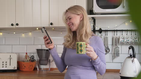 woman using phone and drinking from mug in kitchen