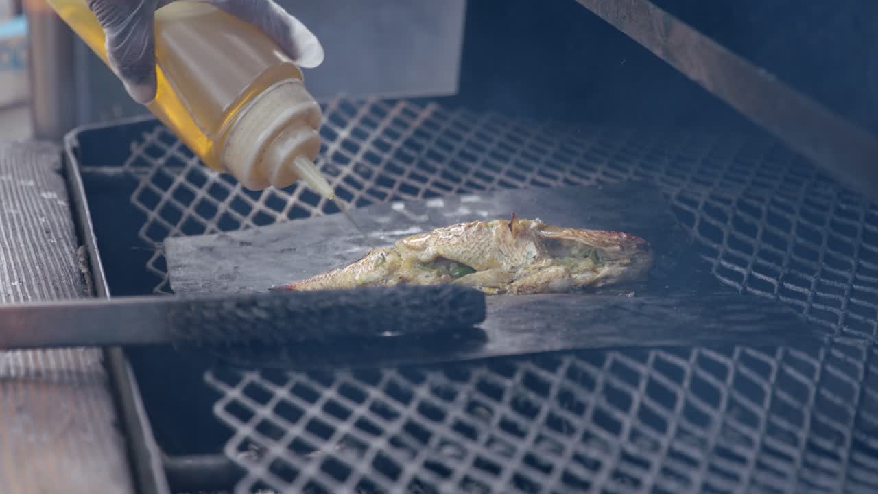 Fish on Metal Plate in BBQ Grill, Adding Oil, Close Up Full Frame Slow Motion