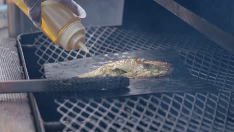 fish on metal plate in bbq grill, adding oil, close up full frame slow motion