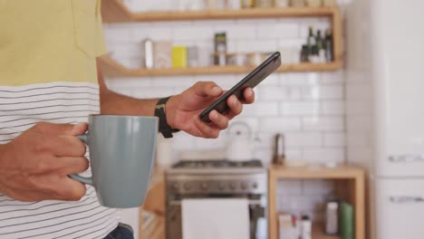 sección media del hombre usando un teléfono inteligente mientras sostiene una taza de café