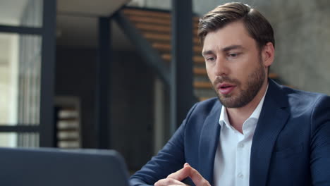 Closeup-focused-businessman-talking-on-laptop-camera-at-remote-office.