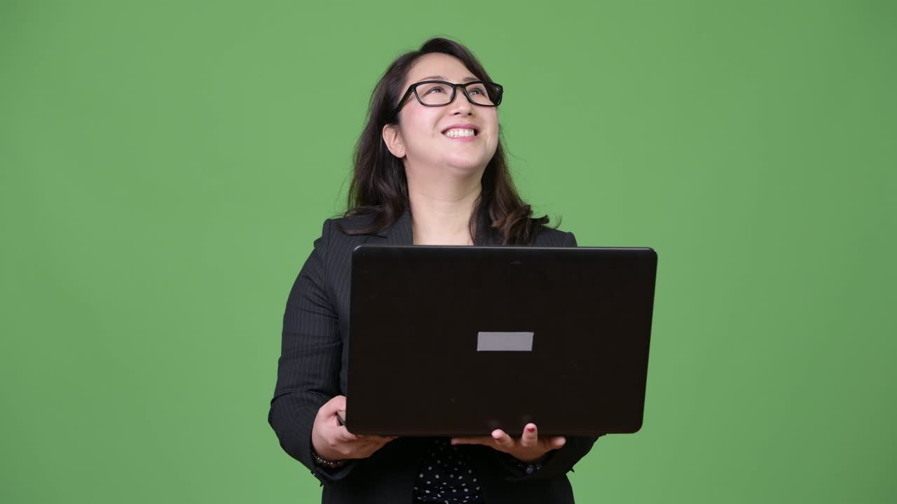 una hermosa mujer de negocios asiática madura usando una computadora portátil contra un fondo verde