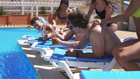 men receiving massage from attractive young girls in bikini lying on coaches by the pool at a beautiful villa and drinking beer