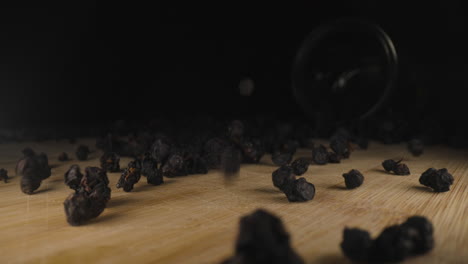 dried european blueberry vaccinium myrtillus falling on wooden table, close up of bilberry fresh organic dehydrated fruit