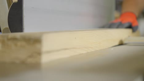 close up shot of worker pushing wooden plank into cutting machine