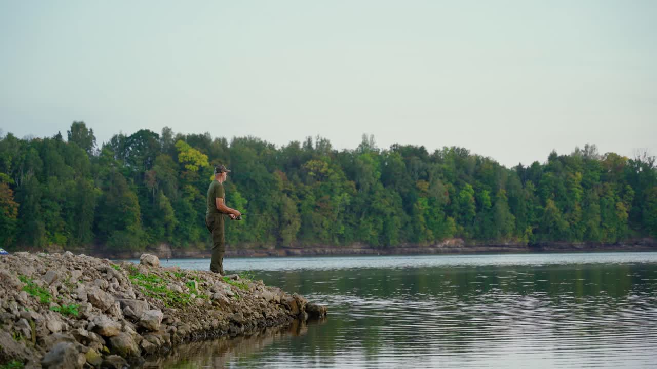 Active senior fishing along the river coast with verdant forest in the background. Enjoying retirement in nature.