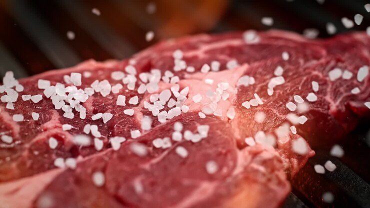 bistec de carne cruda en la parrilla sazonado con sal gruesa en macro y cámara lenta, una fiesta de barbacoa de verano
