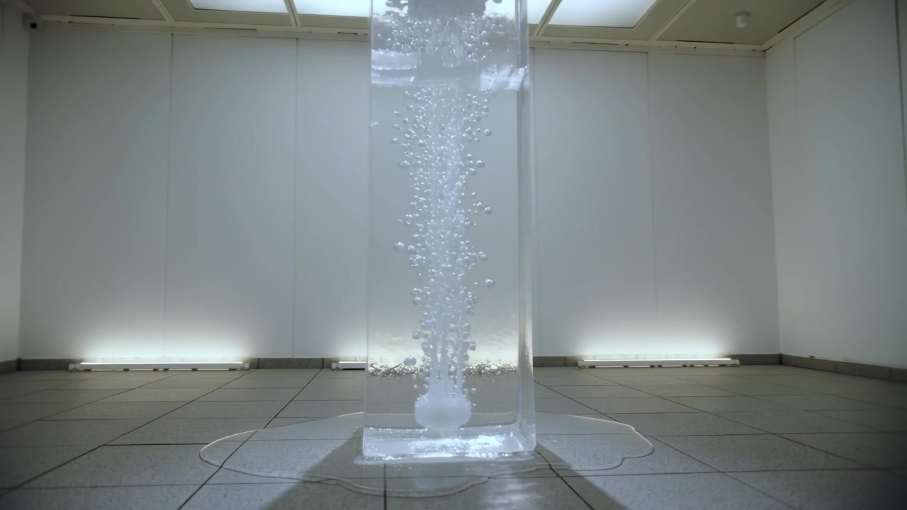 Bubbling tall clear column in gallery, diffuser at base releasing air and puddle expanding