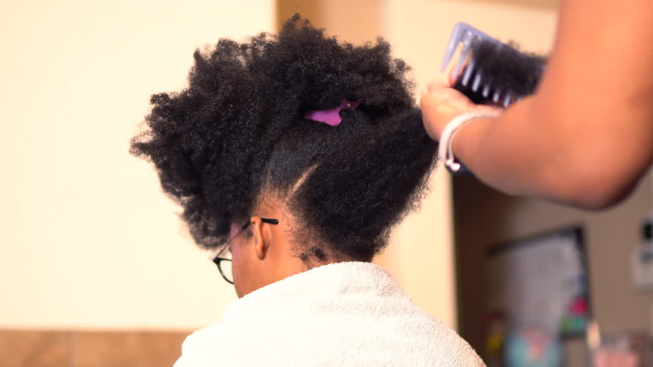 African American mother styling her beautiful teenage daughter's hair in a home salon or kitchen