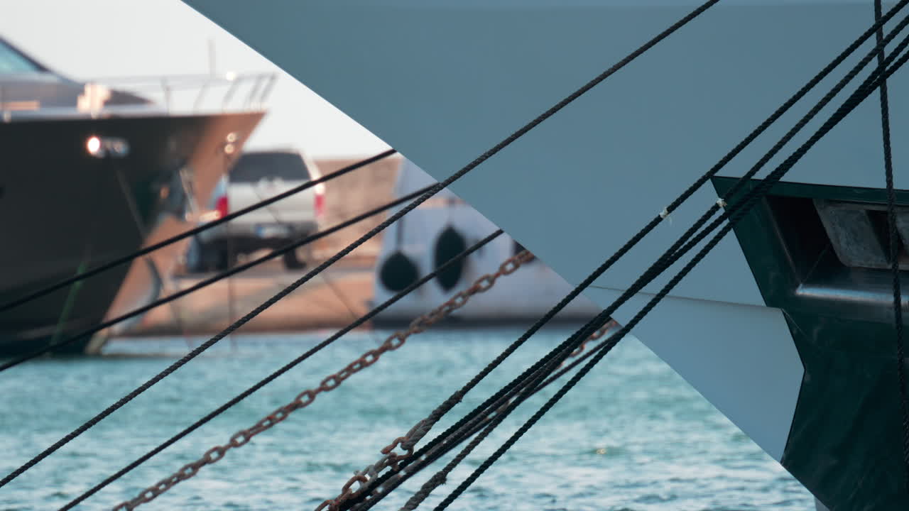 Close up of ropes and metal chains securing a luxury yacht in port, with blurred water and boats in the background