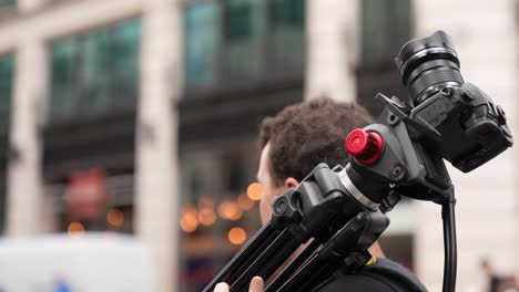 Male-caucasian-videographer-carrying-camera-and-tripod-down-a-road