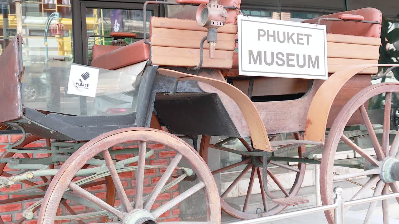A vintage rickshaw is showcased outside Phuket Museum, highlighting historical charm in a bustling Thai street setting
