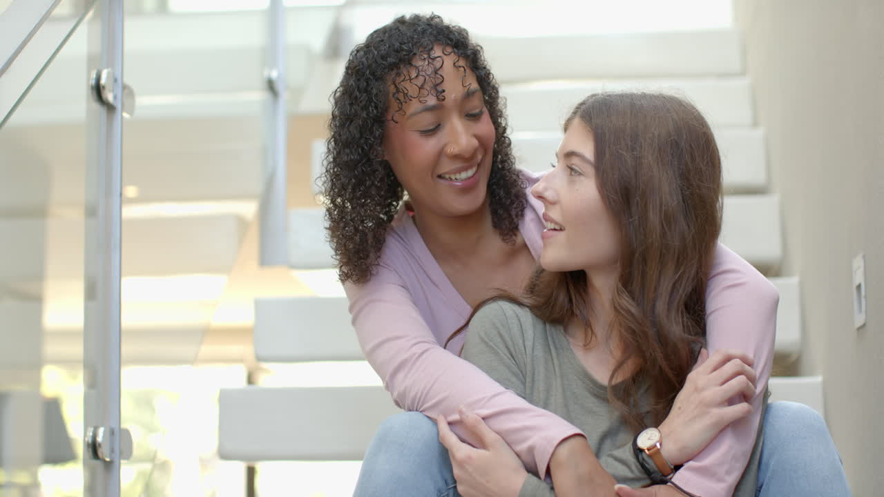 Embracing on staircase, lesbian couple smiling and enjoying time together at home