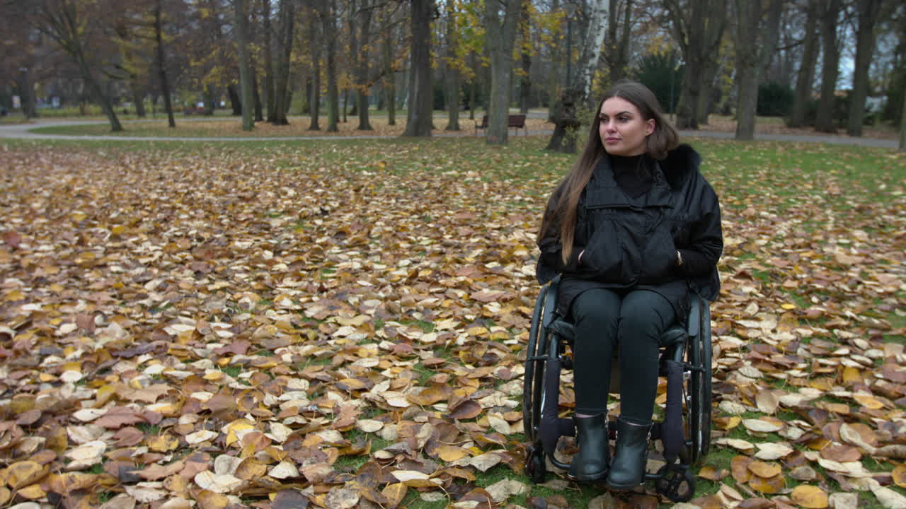 Pretty woman in invalid chair enjoying the autumn time in park with falling colorful leaves