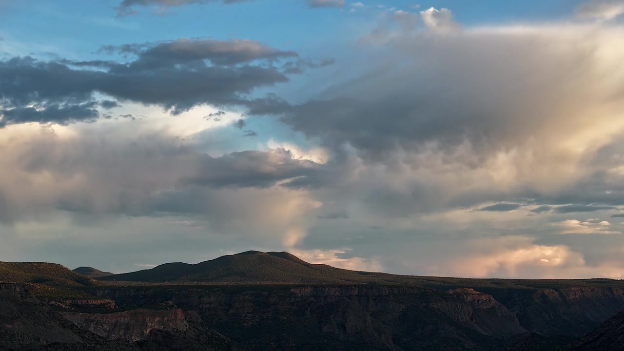 Timelapse 4K UHD con drone che cattura nuvole di pioggia veloci che si muovono su una scura montagna del sud-ovest e una cresta di canyon. La calda luce del tramonto illumina le pesanti formazioni nuvolose e il terreno desertico accidentato