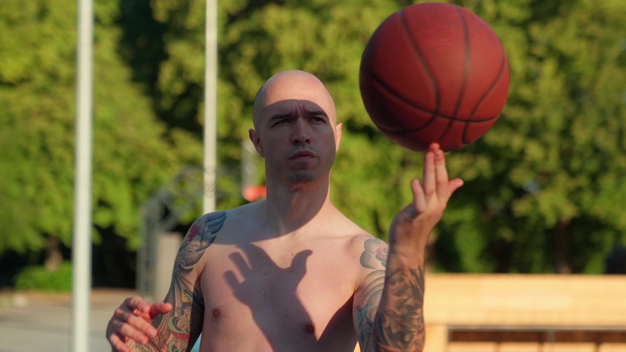 Skaldet tatoveret mand, der dygtigt spinner en basketball på fingeren