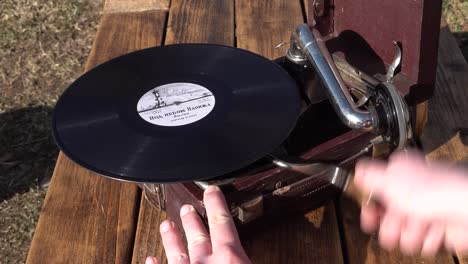 man hand turns on the gramophone mechanism to play vinyl record music. close up