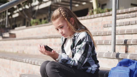 in school, girl sitting on steps using smartphone, concentrating on screen