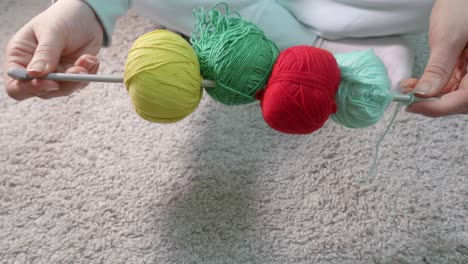 hands demonstrate four balls of different colours on metal knitting needle. close up