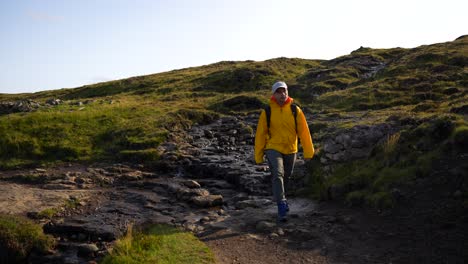 excursionista masculino con chaqueta amarilla cruza el arroyo en leitisvatn, islas feroe