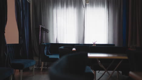 Interior of modern caf with velvet blue seating and a small table by large window. Curtains and minimalist d cor create a calm, peaceful atmosphere. Light filtering through the window