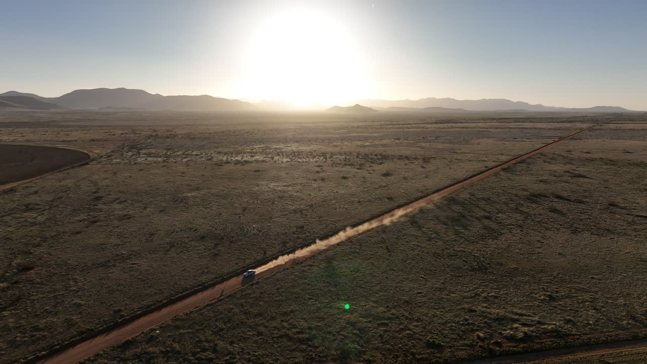 toma aérea de un coche conduciendo por un camino de tierra en willcox, arizona, toma de un dron con montañas en el fondo y polvo detrás del coche