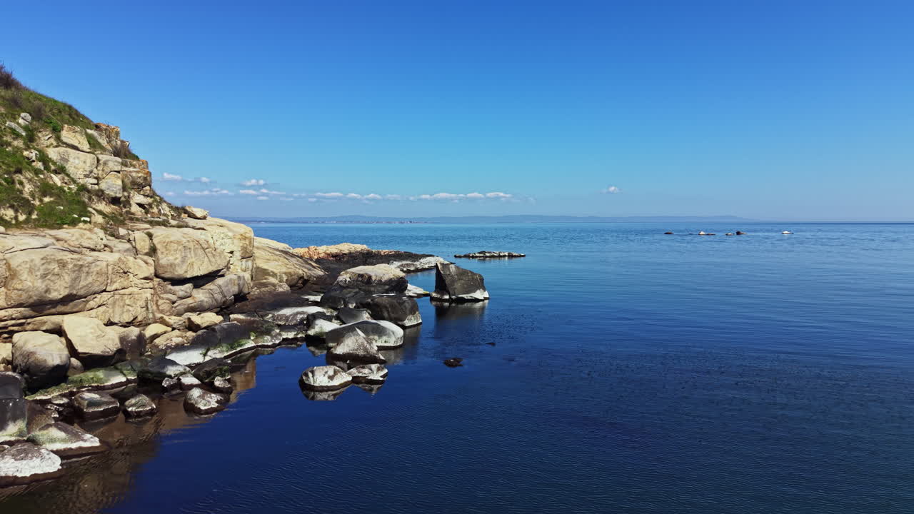 Blick auf eine felsige Küstenlinie am Meer mit klarem blauem Himmel und ruhigem Wasser tagsüber im Freien.