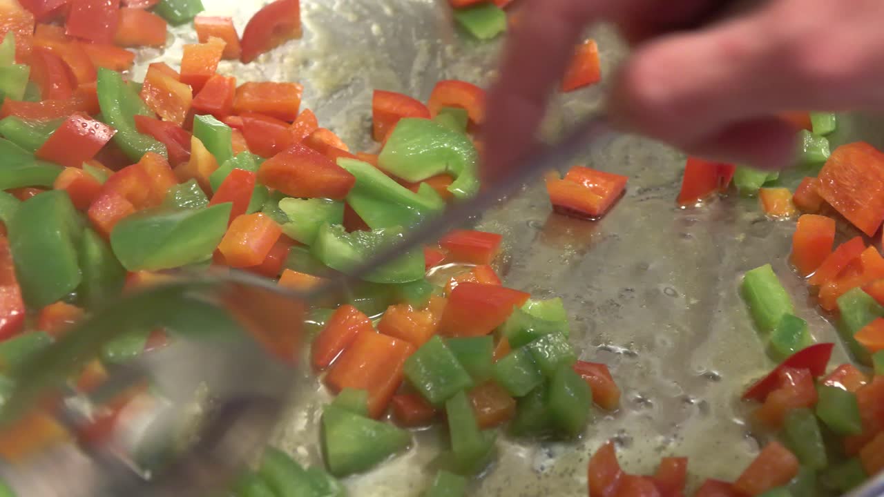 Cooking red and green peppers in a pan with oil - stirring with spoon