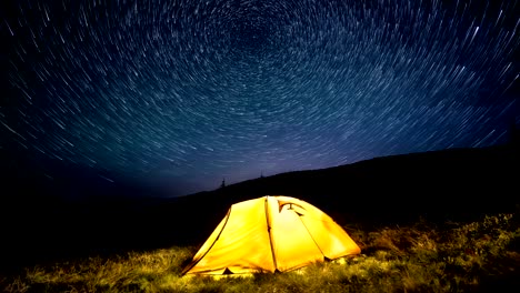 time-lapse. star circles above the night mountains and a glowing camping tent