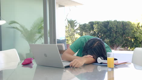 Teenage-Asian-boy-rests-his-head-on-a-desk-at-home-while-studying