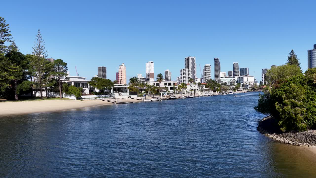 Smooth camera pan across urban canal, luxury homes, boats, and city skyline under bright sunlight