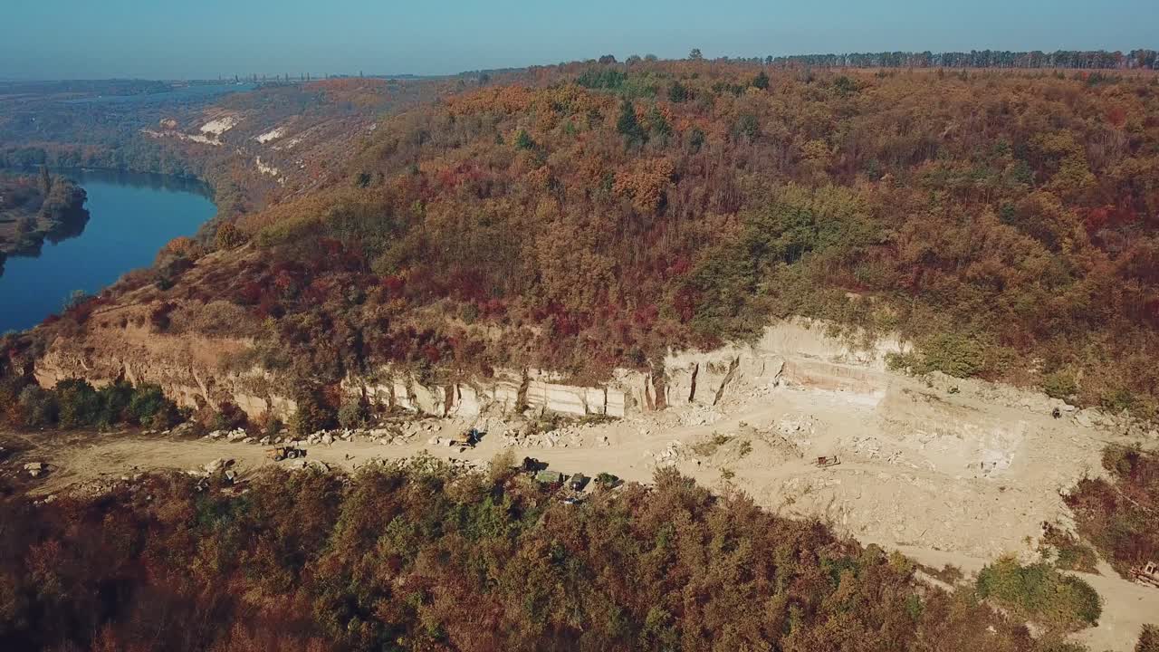 View on the work of equipment in the sand quarry on the background of the forest near the river. Camera movement down. Aerial view