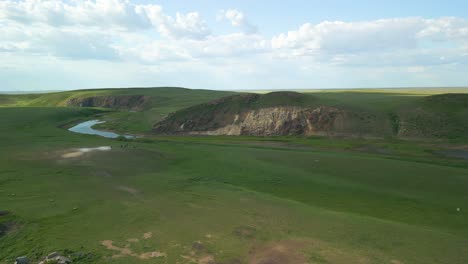 Ruinas-Junto-A-Un-Río-Que-Fluye-A-Través-De-Extensos-Campos-Verdes-En-La-Región-Rural-De-Kazajstán,-Asia-Central---Toma-Aérea-De-Retroceso