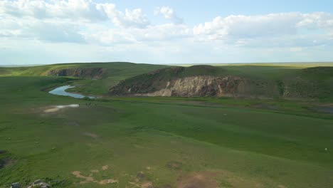 ruinas a lo largo de un río que fluye a través de extensos campos verdes en la región rural de kazajstán, asia central - toma aérea de retroceso