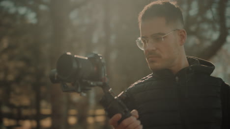 inspirerende millennial content creator die een gemotoriseerde 3-assige elektronische gimbal of steadicam balanceert in de natuur bij zonsondergang