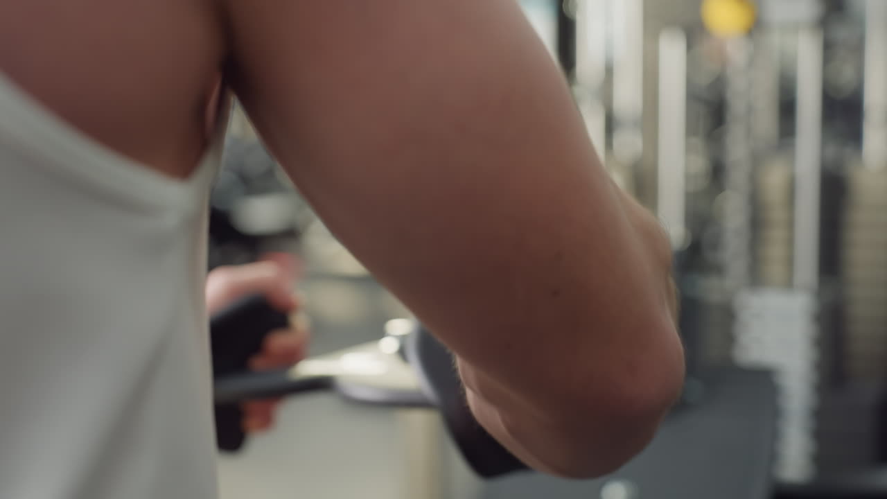 Fitness freak grips handle and pulls rolling machine with focused effort and rhythmic motion, showcasing muscle tension and strength during controlled workout session in modern gym environment