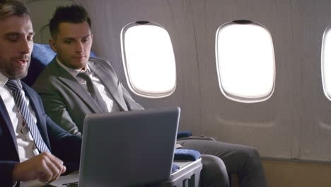 businessmen in suits talking and working on laptop, then shaking hands and making deal while traveling by plane 1