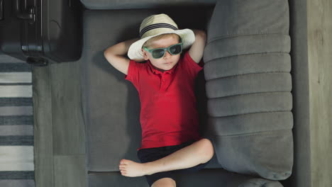 little boy in straw hat relaxes on couch moving with foot