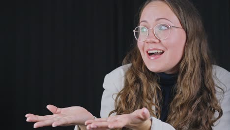 woman quickly grabs face and tosses hands out holding empty space for product on black curtain blackground