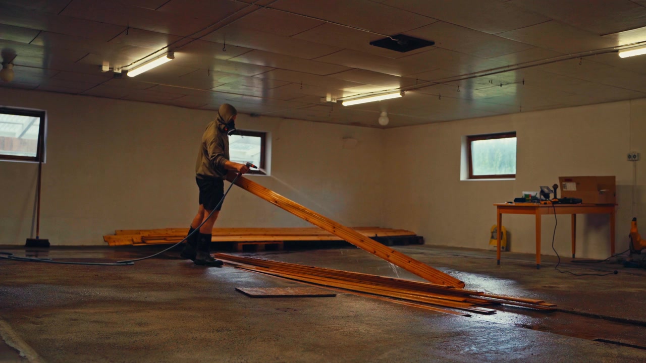 A Person is Cleaning Wooden Boards Indoors Using a Pressure Washer - Static Shot