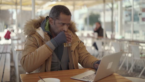 man drinking tea and using laptop in cafe