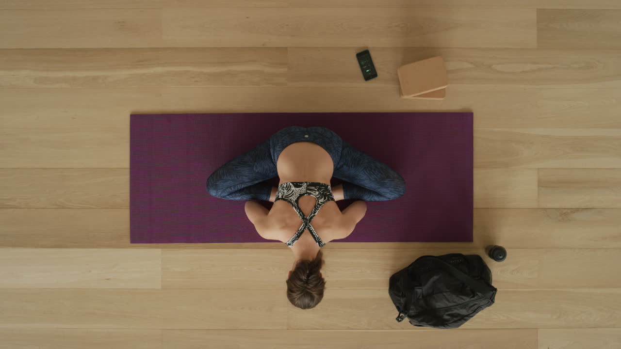 vista dall'alto donna yoga flessibile che pratica la posa della piega in avanti del loto godendo di uno stile di vita sano esercitandosi in allenamento in palestra sul tappetino per esercizi