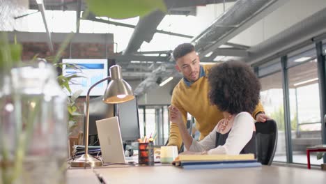 Diverse-man-and-woman-discussing-over-a-computer-at-office