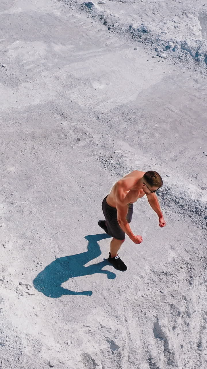 Muscular man on the edge of white hill. Shirtless sportsman shows his strong body on the rocky canyon on the natural summer background. Drone view. Vertical video