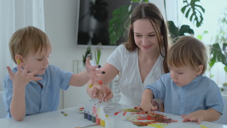 la familia se divierte pintando en el papel con los dedos en la pintura. mamá y dos niños pintan con los dedos en el papel