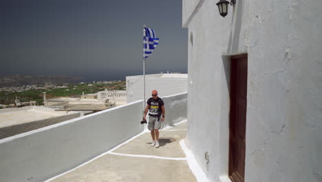 one man holding a camera walks down an alley on a greek island